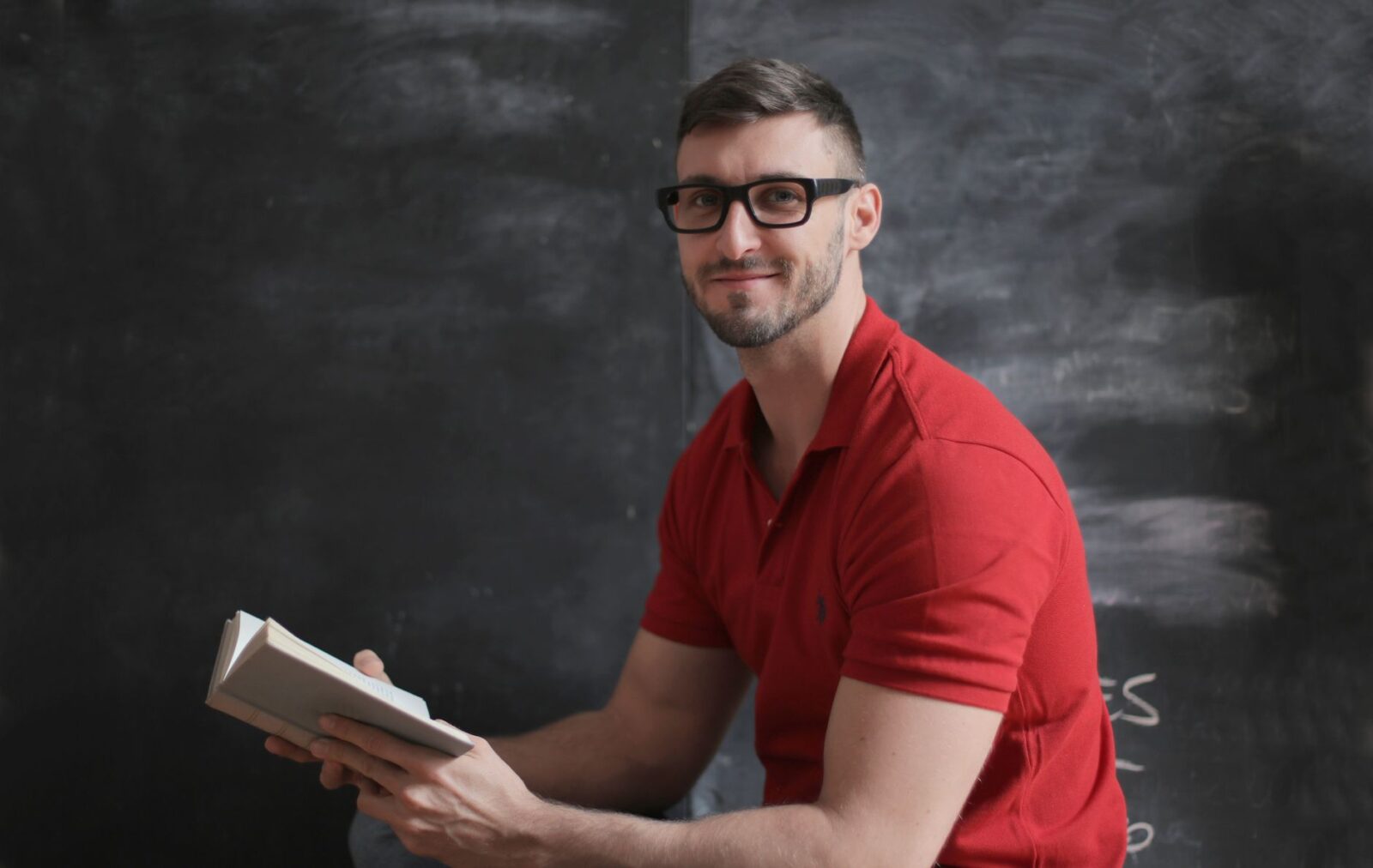Caleb at the chalkboard in his classroom, holding an open book