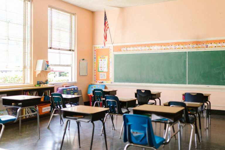 A sunlit classroom with rows of desks, a chalkboard and an American flag