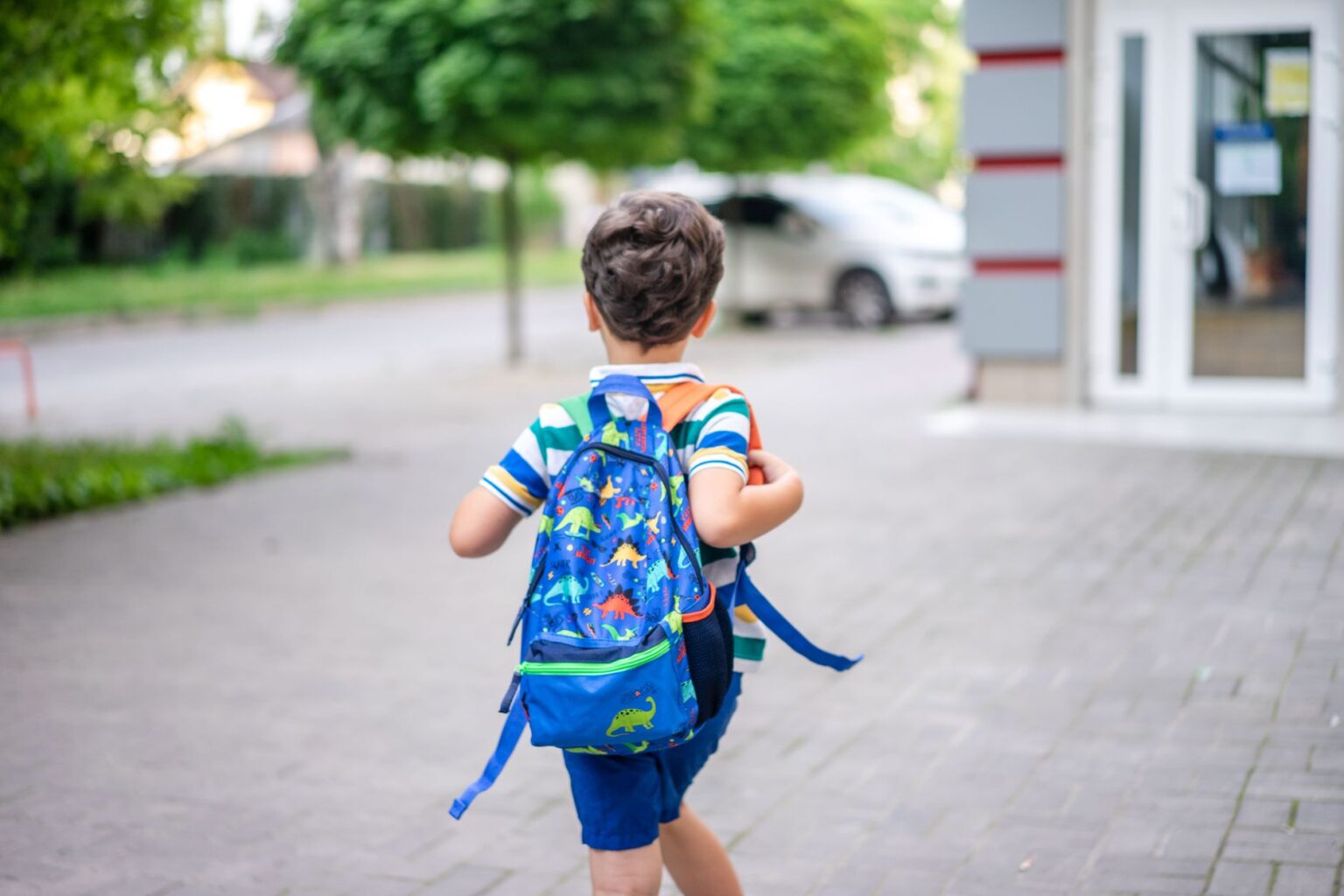 Theo walking to the bus stop with his dinosaur backpack